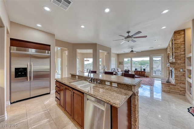 kitchen featuring visible vents, open floor plan, stainless steel appliances, a stone fireplace, and a sink