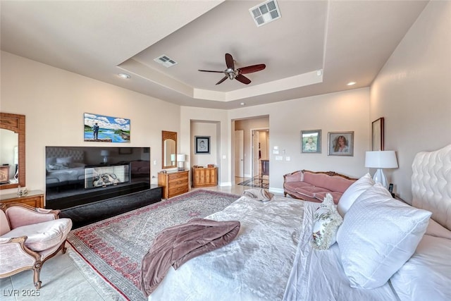 bedroom with a tray ceiling, visible vents, a glass covered fireplace, and baseboards