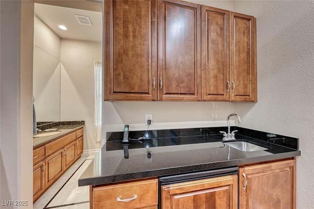 kitchen featuring dark stone countertops, a sink, visible vents, and brown cabinets