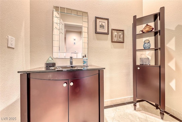 bathroom with a textured wall, baseboards, and vanity