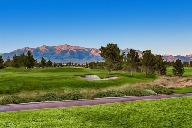 view of property's community with view of golf course, a mountain view, and a lawn