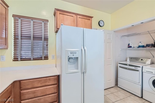 kitchen featuring light tile patterned floors, white refrigerator with ice dispenser, brown cabinetry, light countertops, and washing machine and dryer