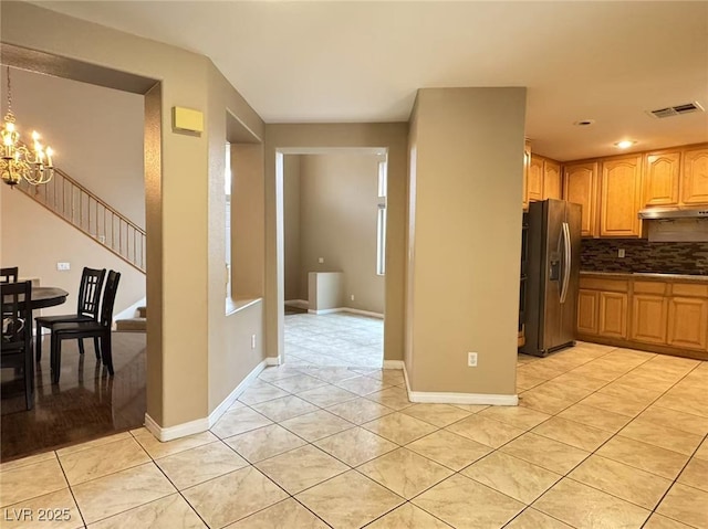 kitchen with light tile patterned floors, stainless steel refrigerator with ice dispenser, decorative backsplash, and an inviting chandelier