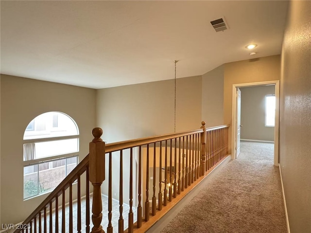 hall with carpet floors, baseboards, visible vents, and an upstairs landing