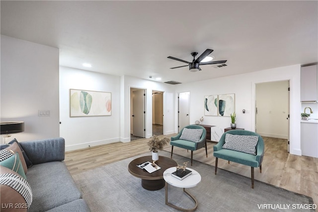 living room with light wood-style floors, visible vents, and ceiling fan