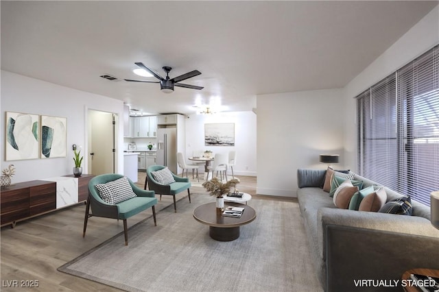 living room with ceiling fan, light wood finished floors, visible vents, and baseboards