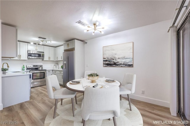 dining space with a textured ceiling, light wood-style flooring, visible vents, baseboards, and an inviting chandelier