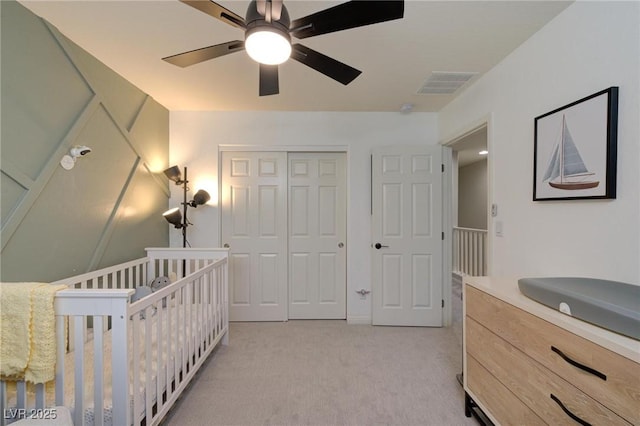 bedroom with ceiling fan, light carpet, visible vents, a closet, and a crib