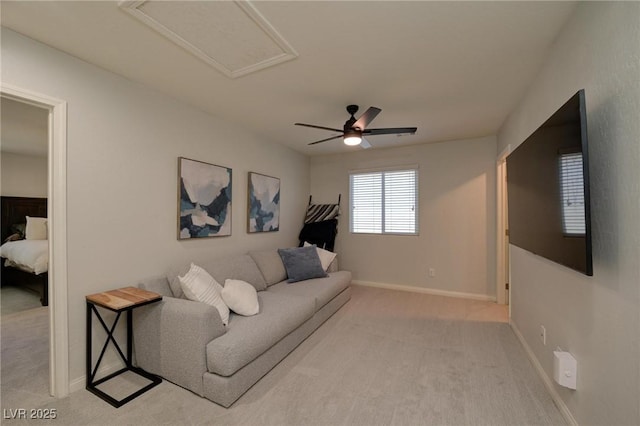 living area featuring attic access, light carpet, baseboards, and a ceiling fan