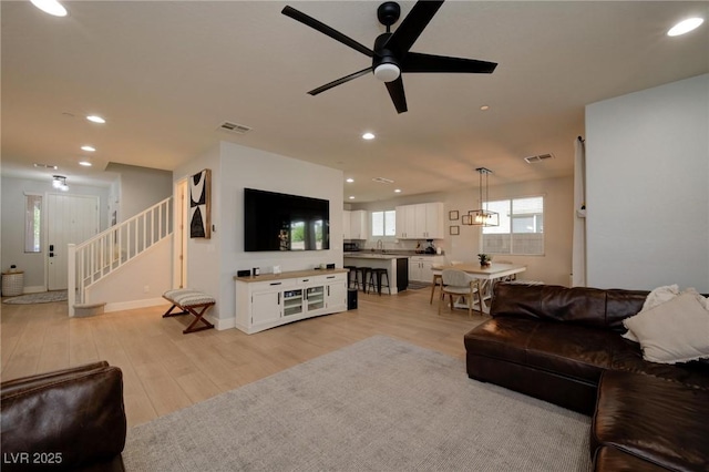 living room featuring light wood-type flooring, visible vents, recessed lighting, and stairs