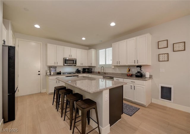 kitchen with a breakfast bar area, a center island, stainless steel appliances, light wood-style floors, and white cabinetry