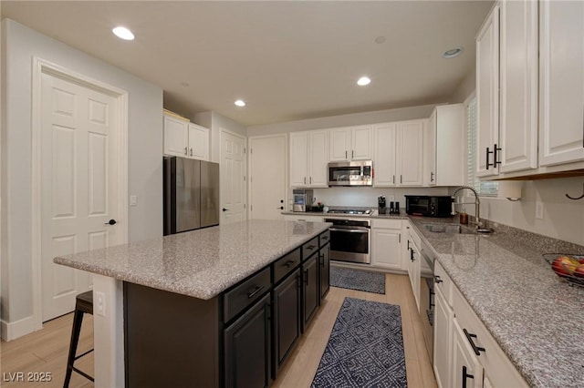 kitchen with stainless steel appliances, a kitchen island, a sink, and white cabinets