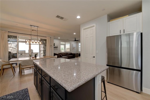 kitchen with visible vents, freestanding refrigerator, white cabinets, a kitchen island, and light stone countertops