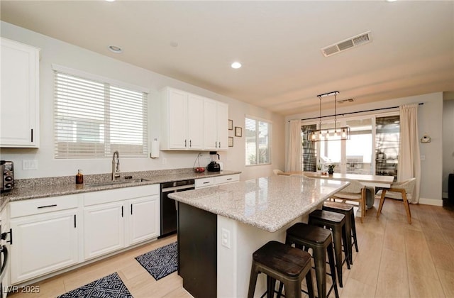 kitchen featuring visible vents, dishwashing machine, a kitchen island, a kitchen bar, and a sink