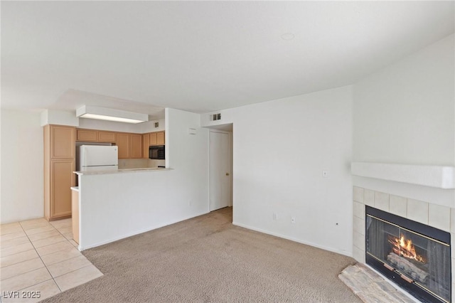 unfurnished living room with light tile patterned floors, a tile fireplace, light colored carpet, visible vents, and baseboards