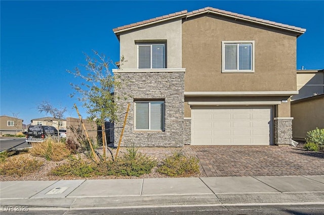 view of front of house with decorative driveway, a tile roof, stucco siding, an attached garage, and stone siding