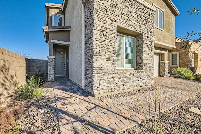 view of side of property featuring a garage, stone siding, fence, and stucco siding