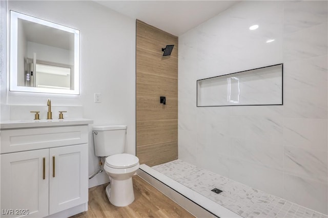 bathroom with vanity, tiled shower, wood finished floors, and toilet