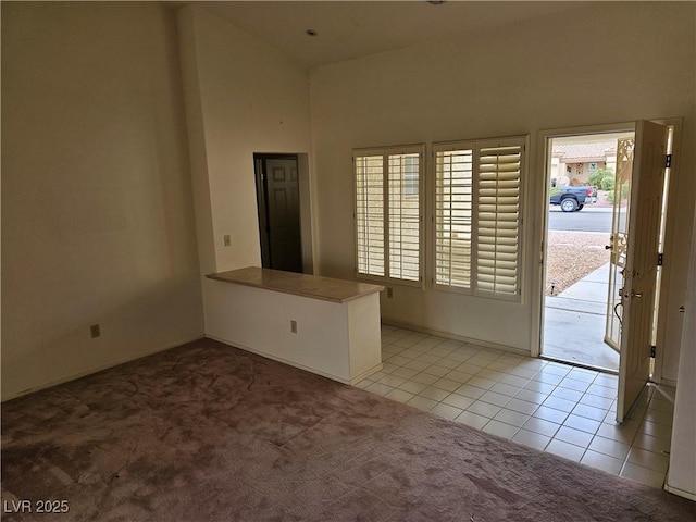 unfurnished room with a healthy amount of sunlight, light carpet, a towering ceiling, and light tile patterned flooring