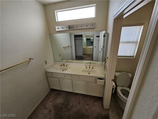 bathroom featuring a textured wall, a sink, toilet, and double vanity