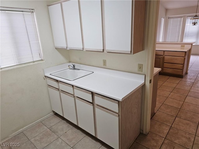 kitchen with light tile patterned flooring, a sink, white cabinetry, light countertops, and an inviting chandelier