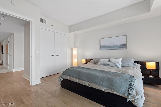 bedroom with light wood-type flooring, a closet, visible vents, and baseboards