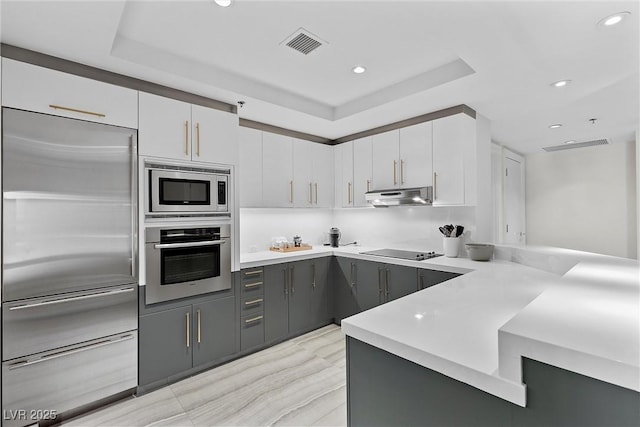 kitchen with visible vents, built in appliances, a peninsula, light countertops, and under cabinet range hood