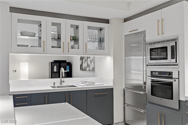 kitchen featuring appliances with stainless steel finishes, light countertops, a sink, and glass insert cabinets