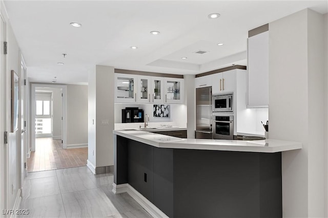 kitchen featuring stainless steel appliances, a peninsula, a sink, and light countertops