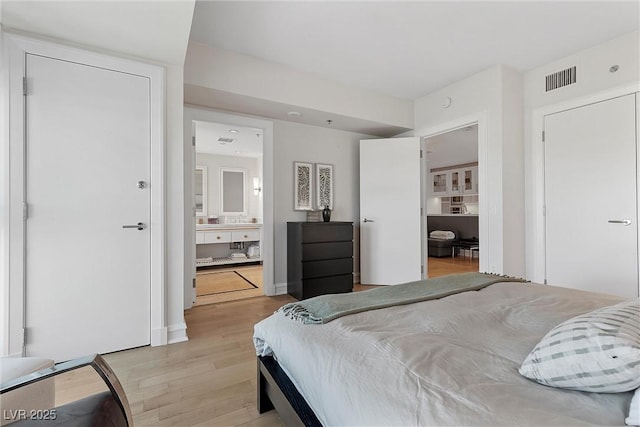 bedroom with light wood finished floors, visible vents, and connected bathroom