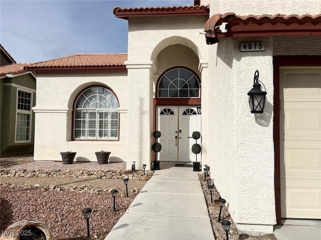 doorway to property featuring a tiled roof, an attached garage, and stucco siding