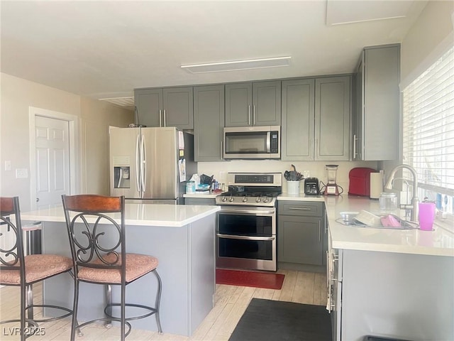 kitchen with stainless steel appliances, a kitchen breakfast bar, light countertops, and gray cabinetry