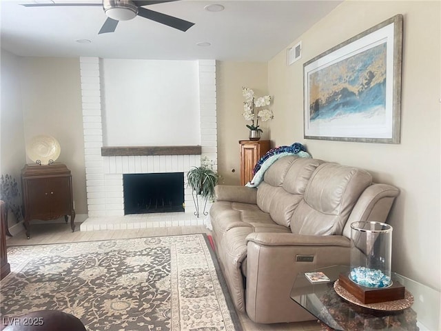 living room with a brick fireplace, visible vents, and a ceiling fan