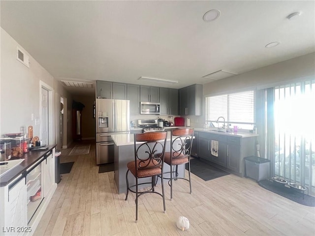 kitchen featuring light wood finished floors, a kitchen island, appliances with stainless steel finishes, a kitchen bar, and a sink