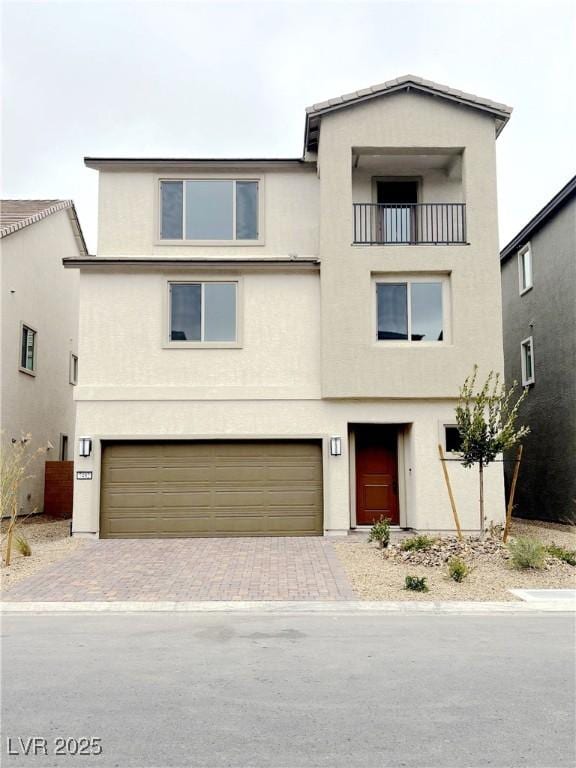 view of property with a garage, decorative driveway, a balcony, and stucco siding