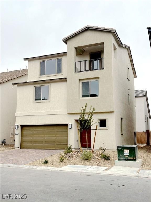 view of property featuring a garage, decorative driveway, a balcony, and stucco siding