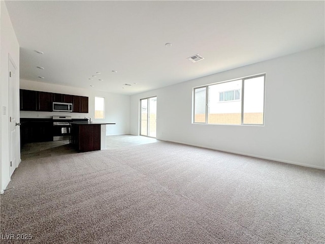 unfurnished living room with baseboards, visible vents, and light colored carpet