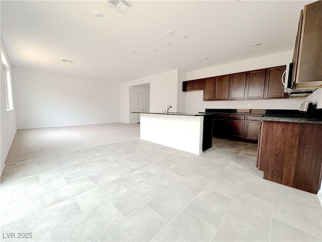 kitchen with dark countertops, visible vents, open floor plan, a sink, and dark brown cabinets