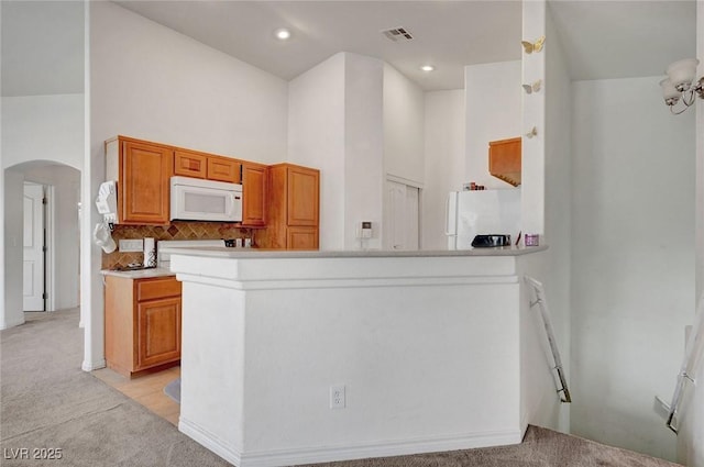 kitchen featuring arched walkways, light colored carpet, visible vents, backsplash, and white appliances