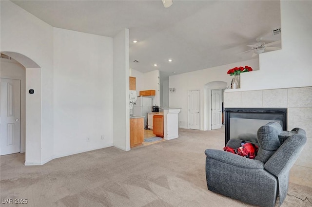 sitting room featuring arched walkways, ceiling fan, light carpet, visible vents, and a tiled fireplace