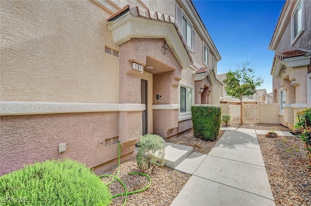 view of exterior entry with a gate, fence, and stucco siding