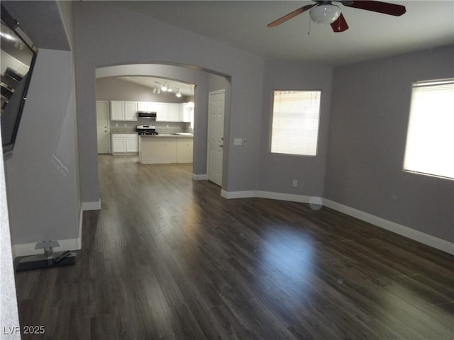 unfurnished living room featuring arched walkways, ceiling fan, dark wood-style flooring, and baseboards