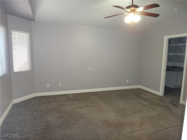 spare room featuring a ceiling fan, dark colored carpet, lofted ceiling, and baseboards