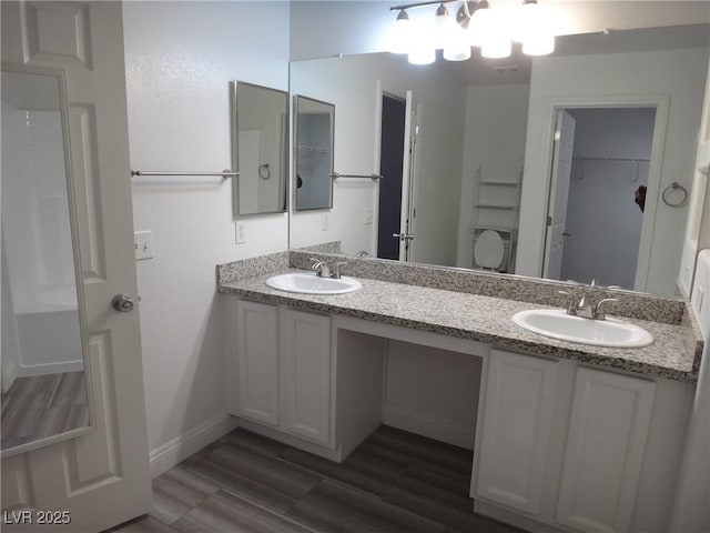 bathroom featuring double vanity, baseboards, a sink, and wood finished floors