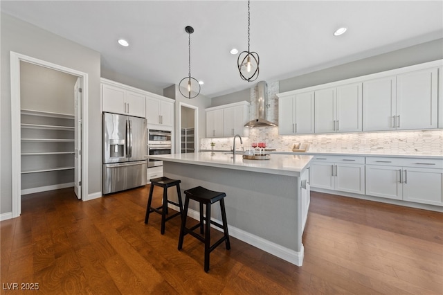 kitchen featuring wall chimney exhaust hood, a breakfast bar, stainless steel appliances, light countertops, and white cabinetry