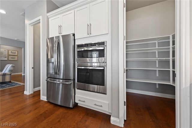 kitchen with baseboards, appliances with stainless steel finishes, white cabinets, and dark wood-style flooring