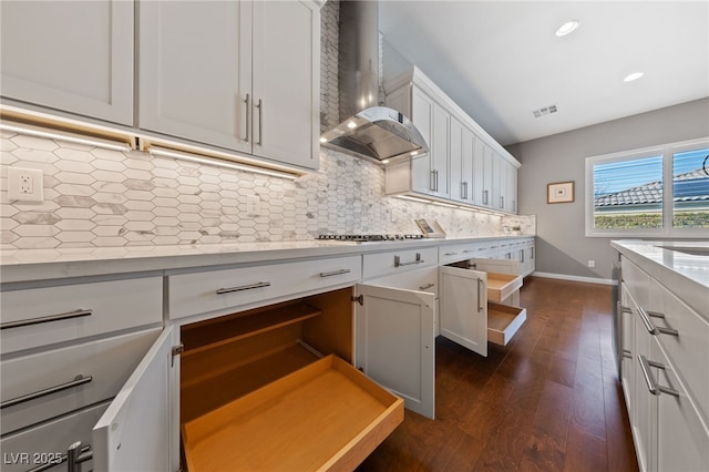 kitchen featuring visible vents, baseboards, wall chimney range hood, backsplash, and dark wood finished floors