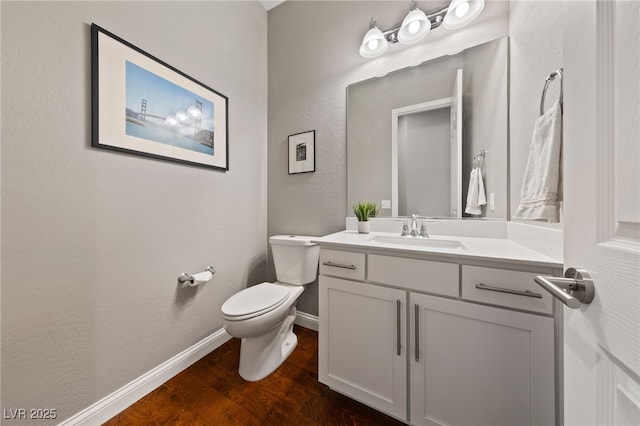 half bath with vanity, wood finished floors, toilet, and baseboards