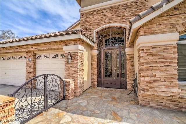 property entrance with a garage, stone siding, and a gate