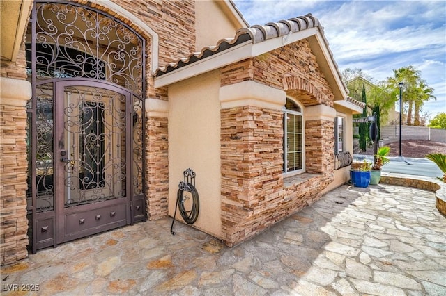 doorway to property with stucco siding, stone siding, and a tiled roof